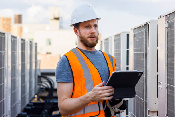 Rooftop air conditioning system inspection. Caucasian white workers check units and log the result with a portable computer.